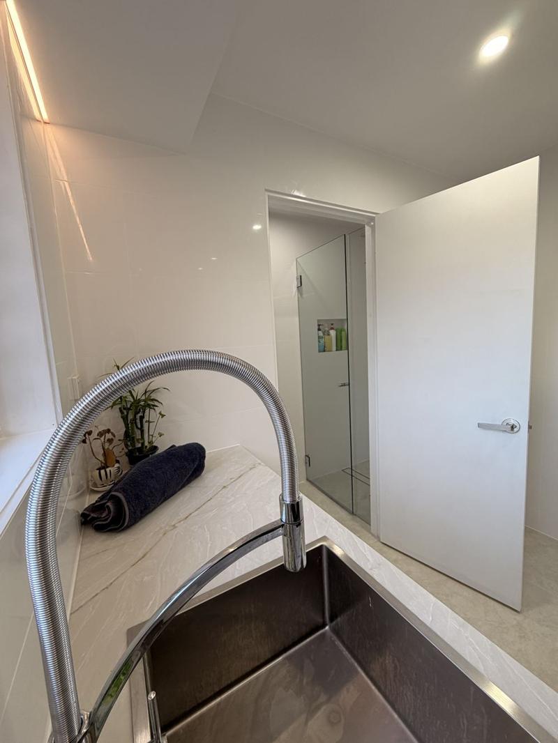 View from the laundry bench through a white door to a frameless glass shower